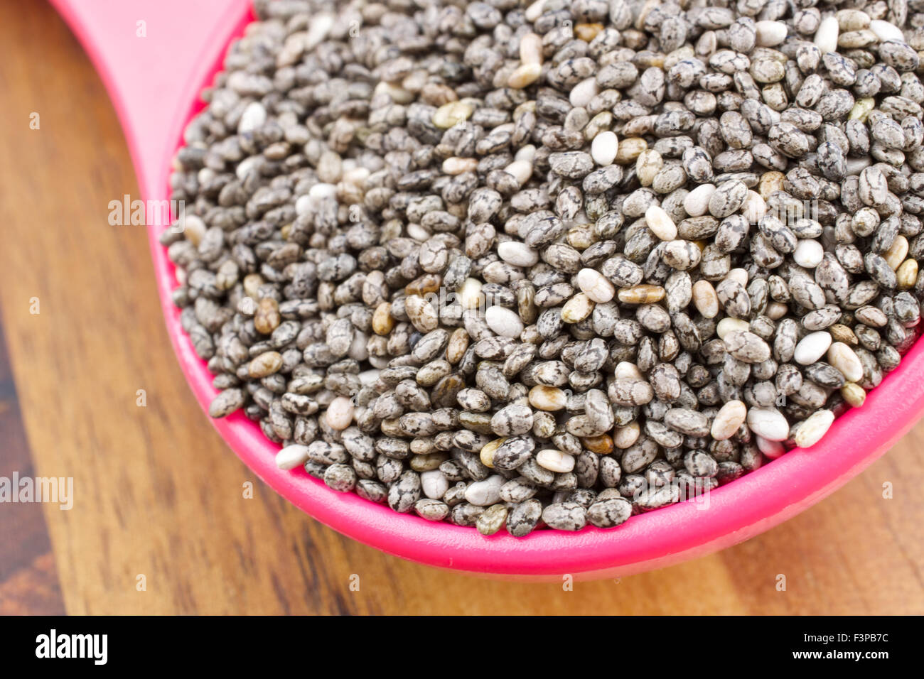 Semi di Chia in cucchiaio colorati su un sfondo di legno Foto Stock