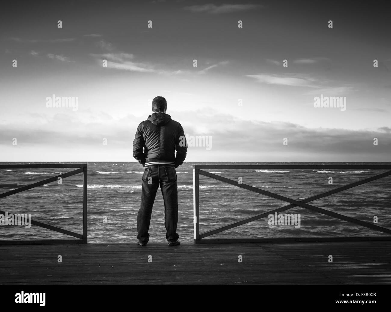 Giovane uomo che guarda sul mare dal molo in legno. Vista posteriore, foto in bianco e nero Foto Stock