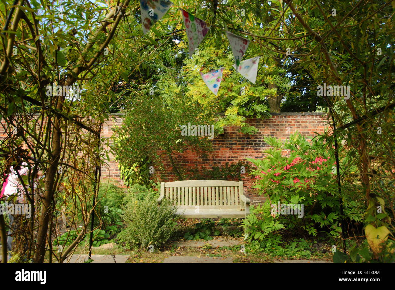 Una panca in legno è incorniciata da un arco fatto di Willow e decorate con bunting in un giardino murato, tarda estate, England, Regno Unito Foto Stock