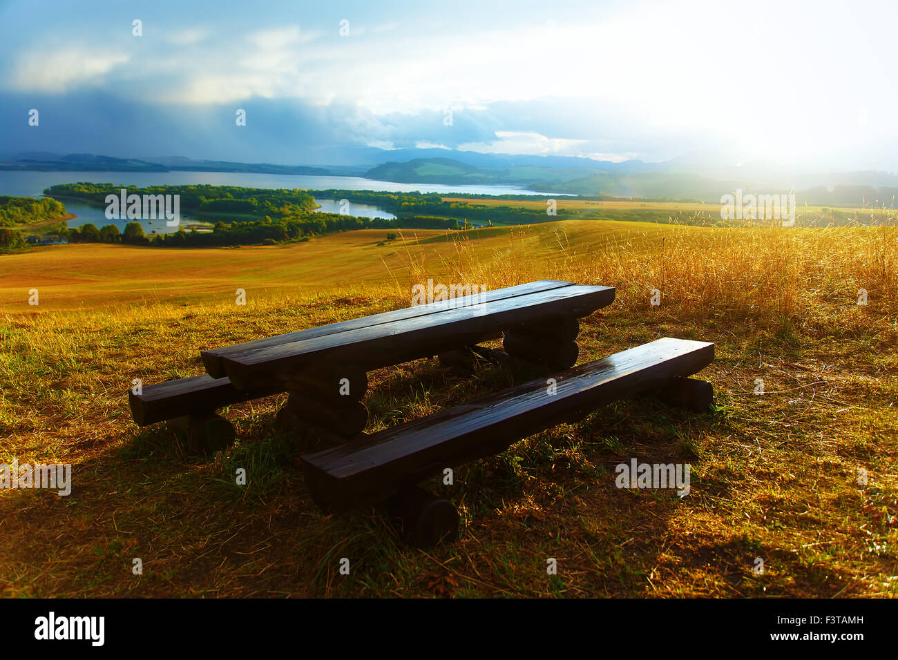 Bellissimo paesaggio. Panca in legno nel prato, affacciato sul lago e le montagne con bellissimo cielo molto nuvoloso Foto Stock