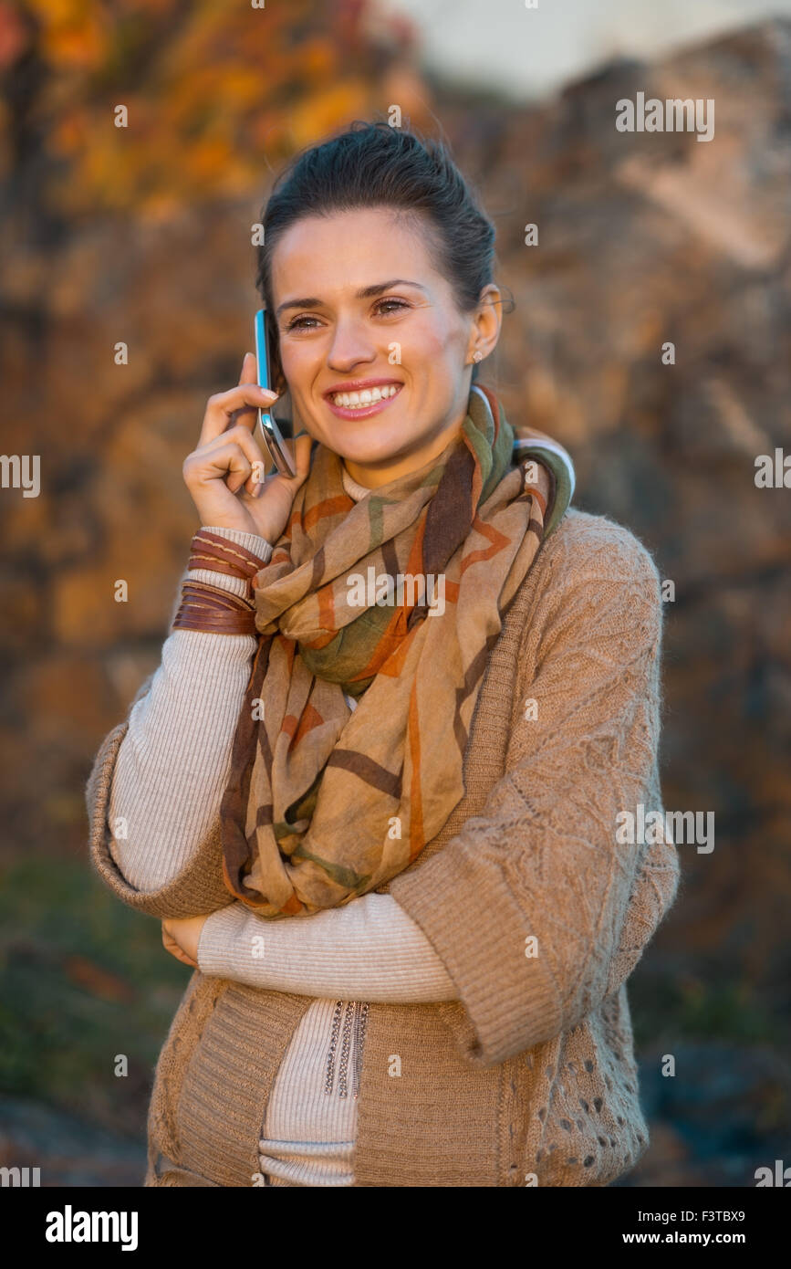 Elegante sorridente i capelli castani Donna che parla il telefono cellulare mentre si cammina in serata in autunno park Foto Stock