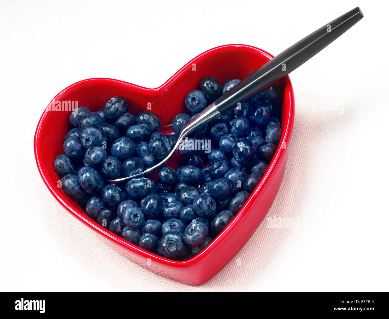 I mirtilli cuore della salute alimentare cuore concetto / i mirtilli in un cuore rosso piatto sagomato con design contemporaneo cucchiaio su sfondo bianco Foto Stock