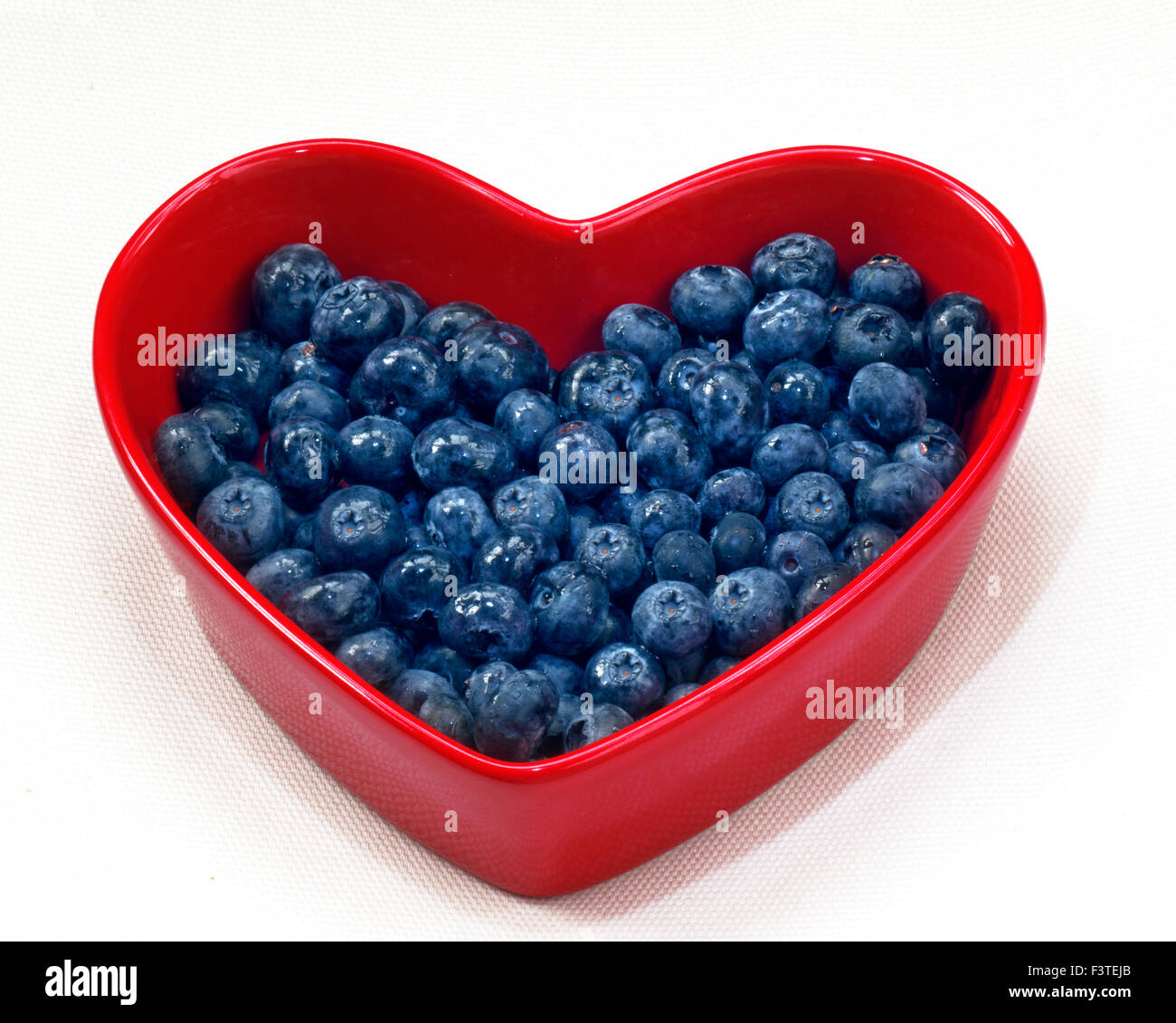I mirtilli cuore piatto della salute alimentare cuore concetto / i mirtilli in un cuore rosso piatto sagomato su sfondo bianco Foto Stock