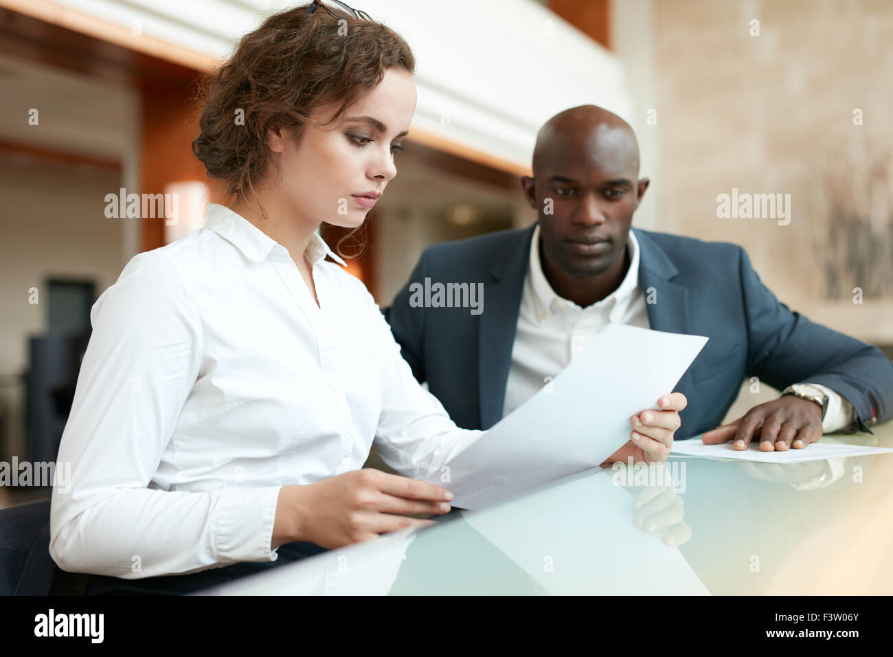 Due giovani uomini di affari seduti al bar a lavorare. Business donna la lettura di una carta con il suo collega seduto da. Foto Stock