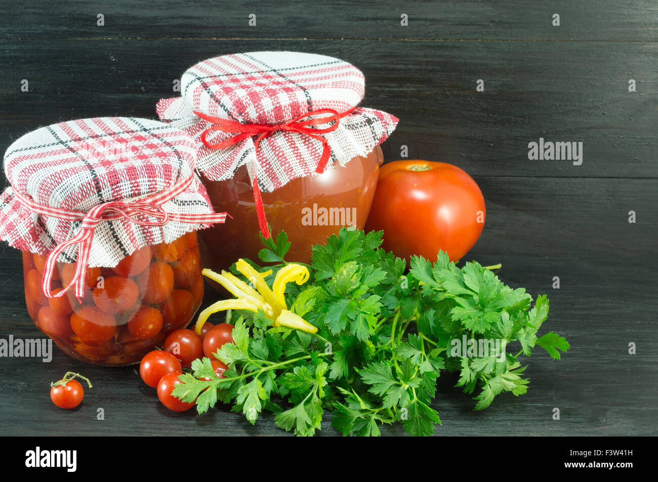 Vasetti di ketchup fatti in casa e pomodoro ciliegino accanto a freschi pomodori ciliegia su sfondo scuro Foto Stock