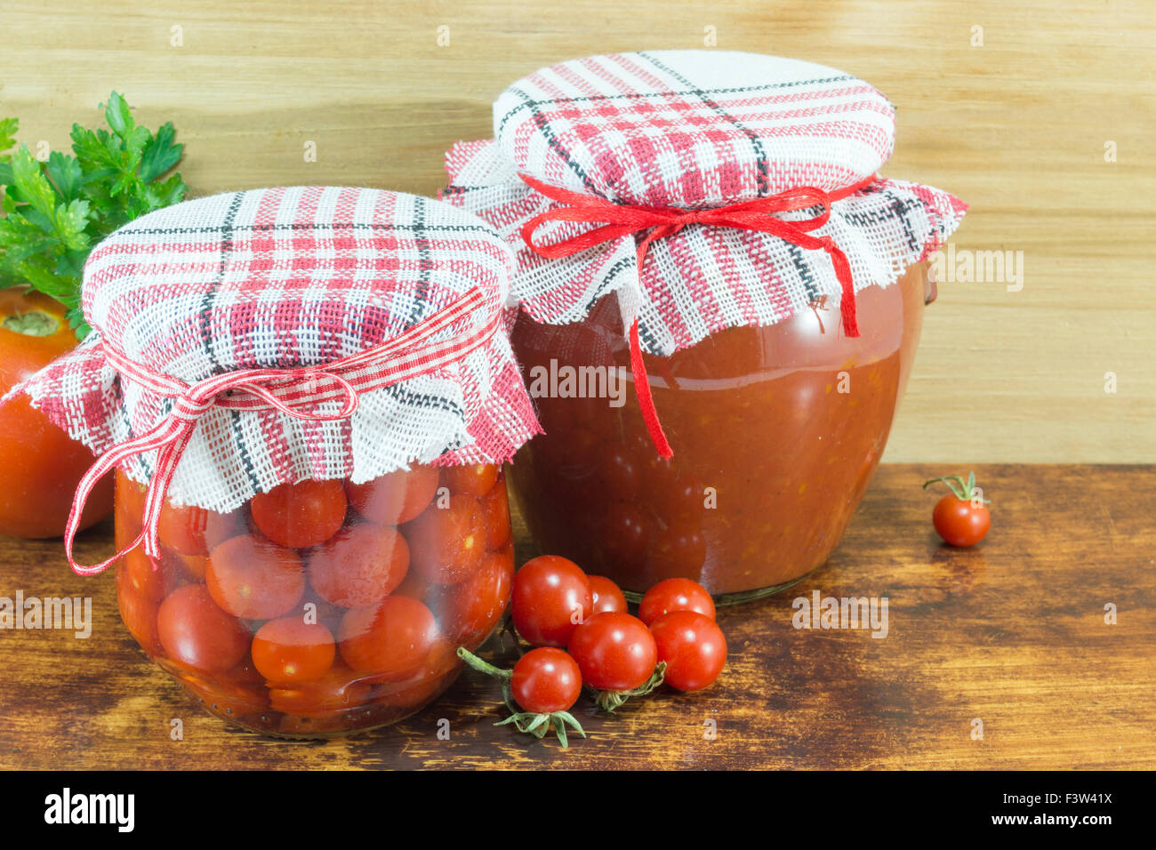 Vasetti di ketchup fatti in casa e pomodoro ciliegino accanto a freschi pomodori ciliegia su sfondo di legno Foto Stock