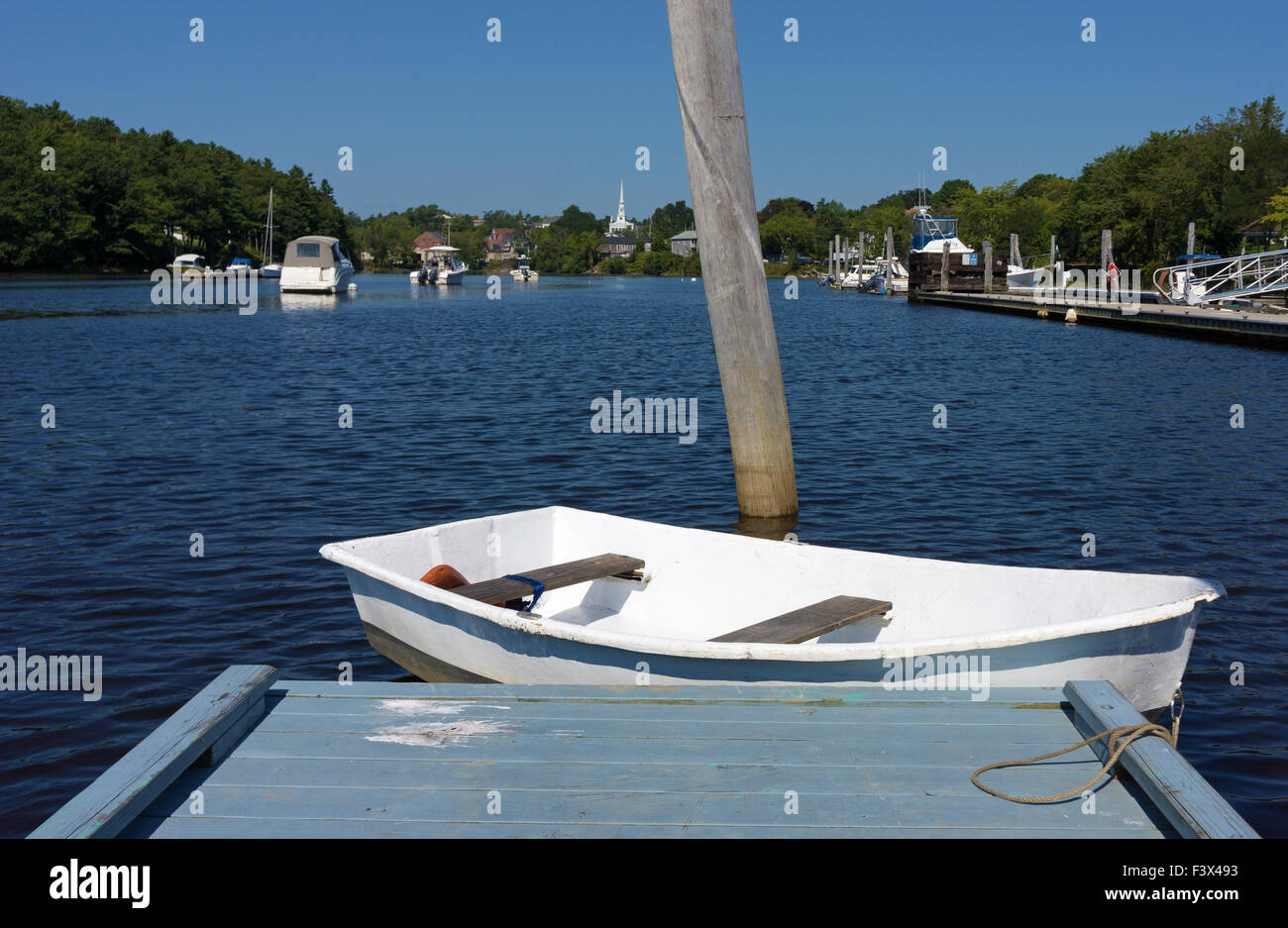 Un bianco dinghy floating alla fine di un dock con barche e la lontana città di Ellsworth, Maine in estate. Foto Stock