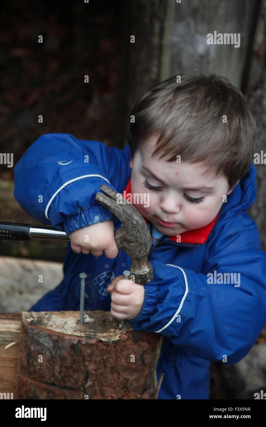 Piccolo Ragazzo per imparare a utilizzare un martello per battere chiodo in legno Foto Stock