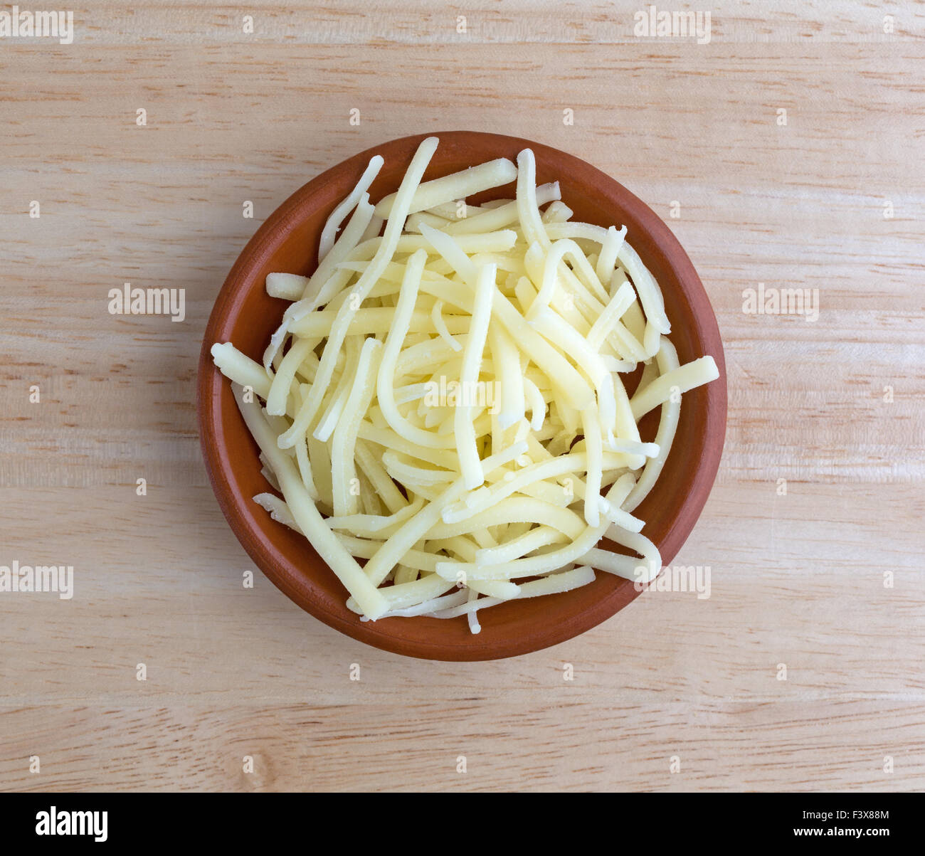 Vista dall'alto di una porzione di delicato naturale formaggio cheddar in una piccola ciotola sulla cima di un legno tavolo illuminato con luce naturale. Foto Stock