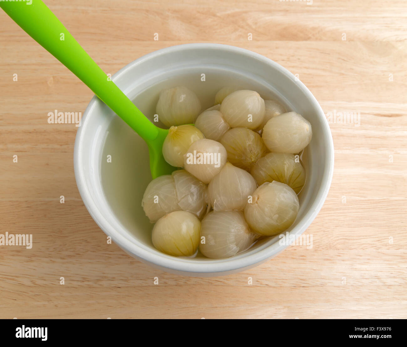 Una ciotola riempita con cotte cipolle piccole nel liquido con un cucchiaio di verde inserita su una tavola di legno top Foto Stock