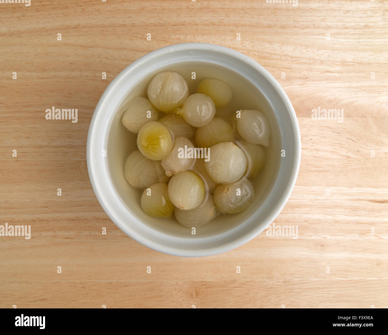 Vista dall'alto di una ciotola riempita con cotte piccole cipolle in liquido su una tavola di legno top illuminato con luce naturale. Foto Stock