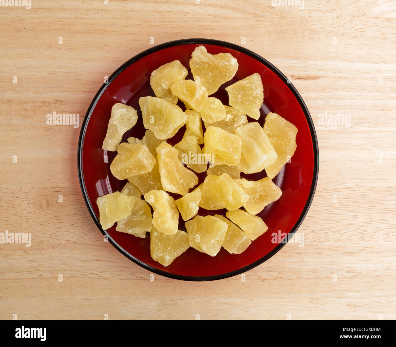 Vista dall'alto di una porzione di essiccato confetti di ananas in pezzi su un piatto di colore rosso sulla cima di una tavola di legno alto. Foto Stock