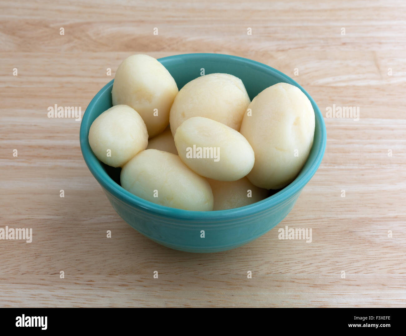 Una piccola ciotola riempita con tutta la patate bianche su una tavola di legno top illuminato con luce naturale. Foto Stock