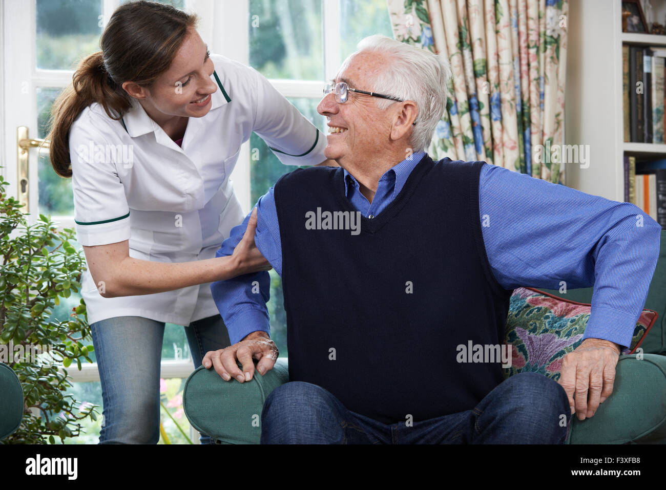 Lavoratore di cura di aiutare l uomo Senior per arrivare fino al di fuori della sedia Foto Stock