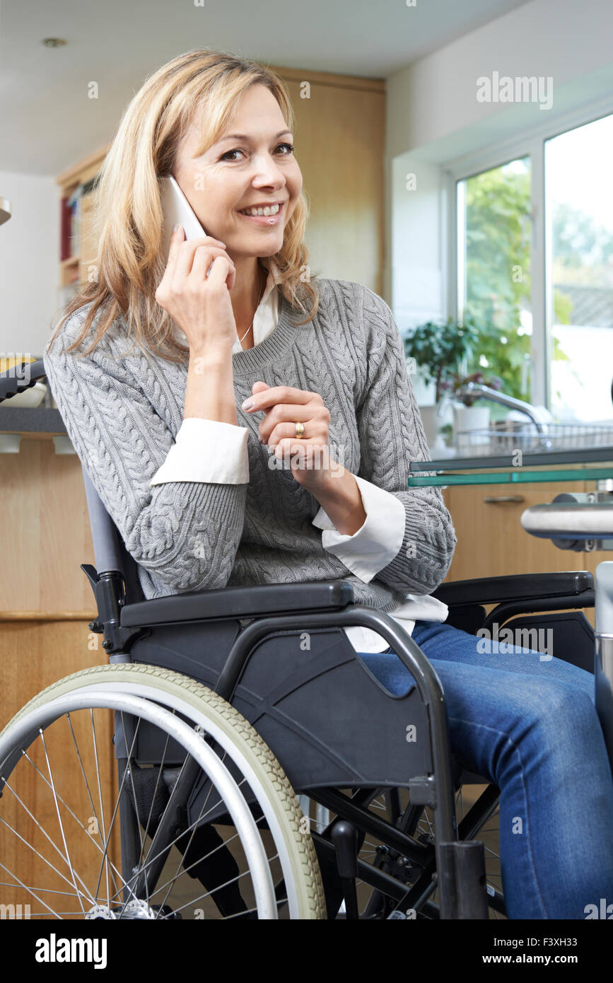 Donna disabile in carrozzella effettuare una chiamata sul telefono cellulare a casa Foto Stock