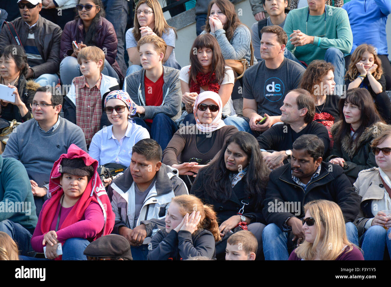 Un gruppo di persone multietniche di tutte le età, ampio e diversificato, che si siedono all'esterno su bleachers in cemento che reagiscono a guardare artisti di strada che si esibiscono negli Stati Uniti Foto Stock