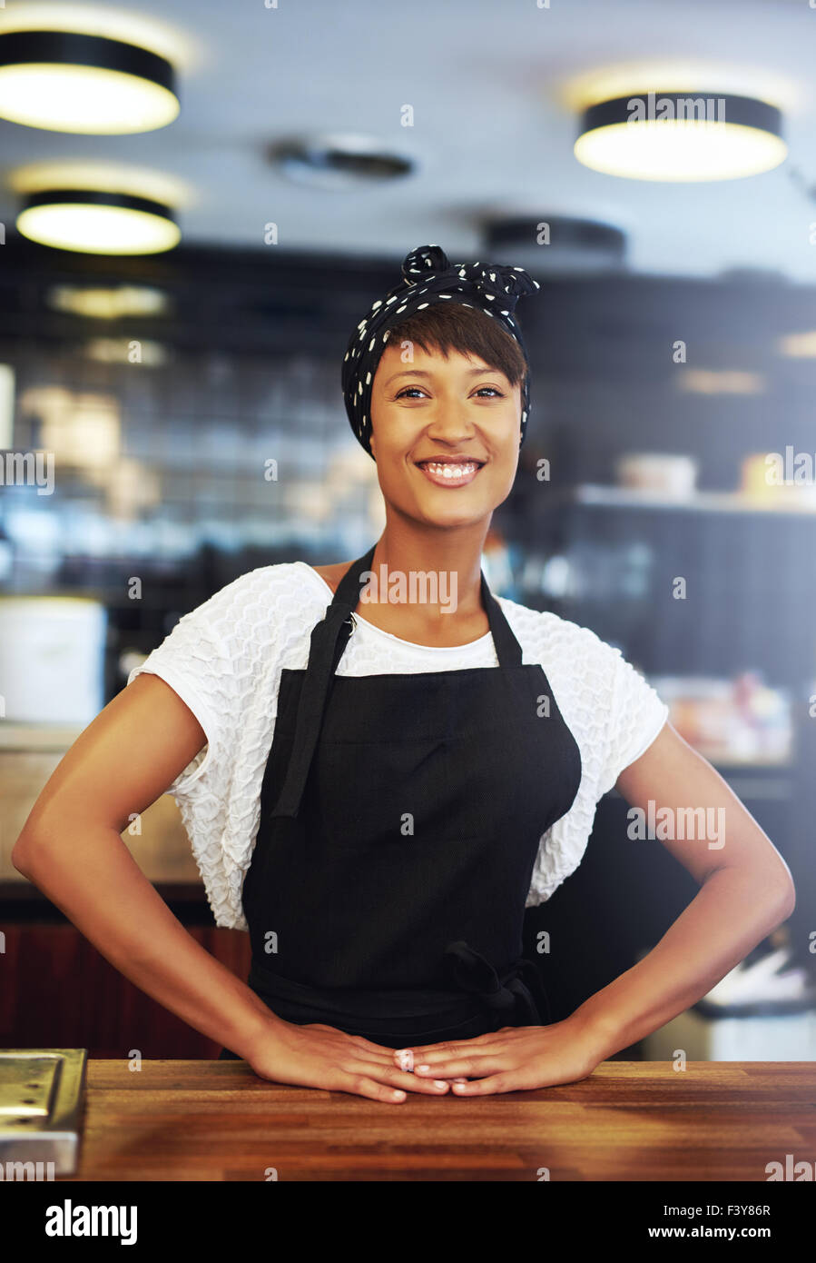 Fiducioso il successo giovane titolare di una piccola azienda in piedi dietro il contatore nella sua caffetteria dando alla telecamera un felice welcomi Foto Stock