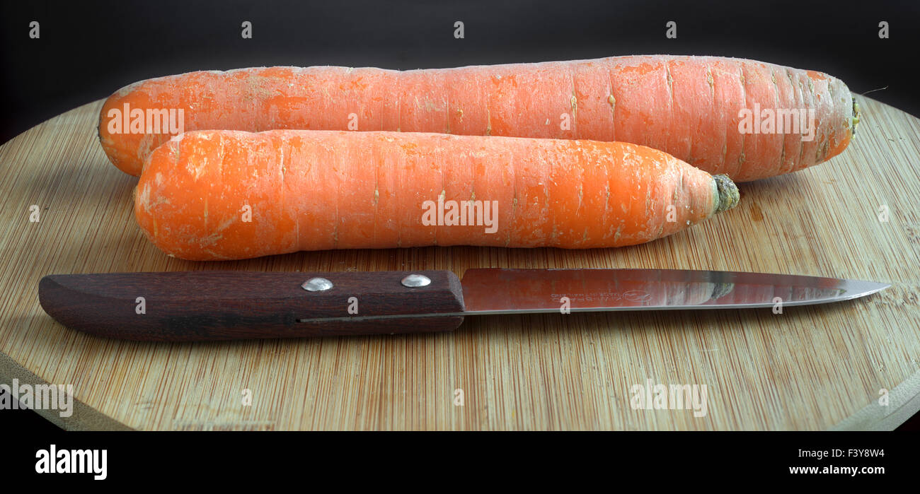 Le carote e un coltello su un pannello di legno Foto Stock