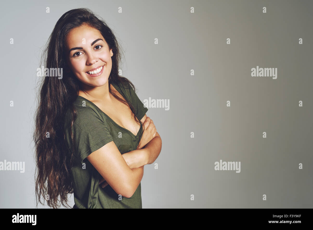 Ritratto di casual donna alla moda con le braccia incrociate e sorridente, su sfondo grigio Foto Stock