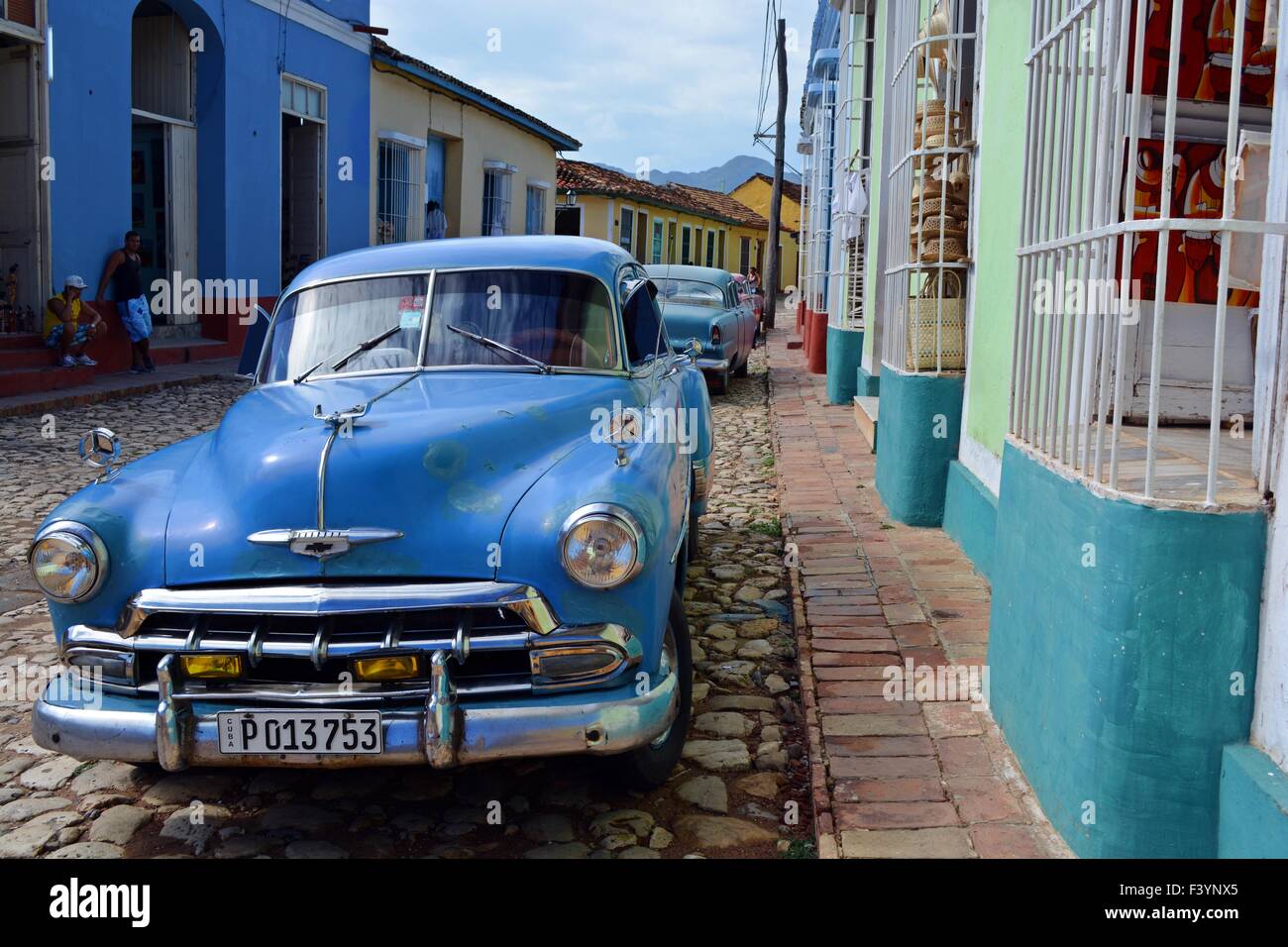 Tranquilla strada colorato in Trinidad Cuba con un paio di ragazzi locale appendere fuori e parcheggiata auto d'epoca Foto Stock