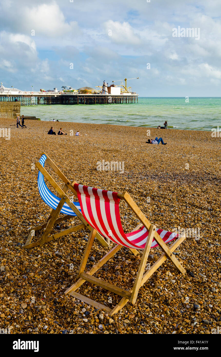 Due sedie a sdraio sulla spiaggia unico a Brighton e Hove con il Molo di Brighton in distanza, East Sussex, Inghilterra. Foto Stock