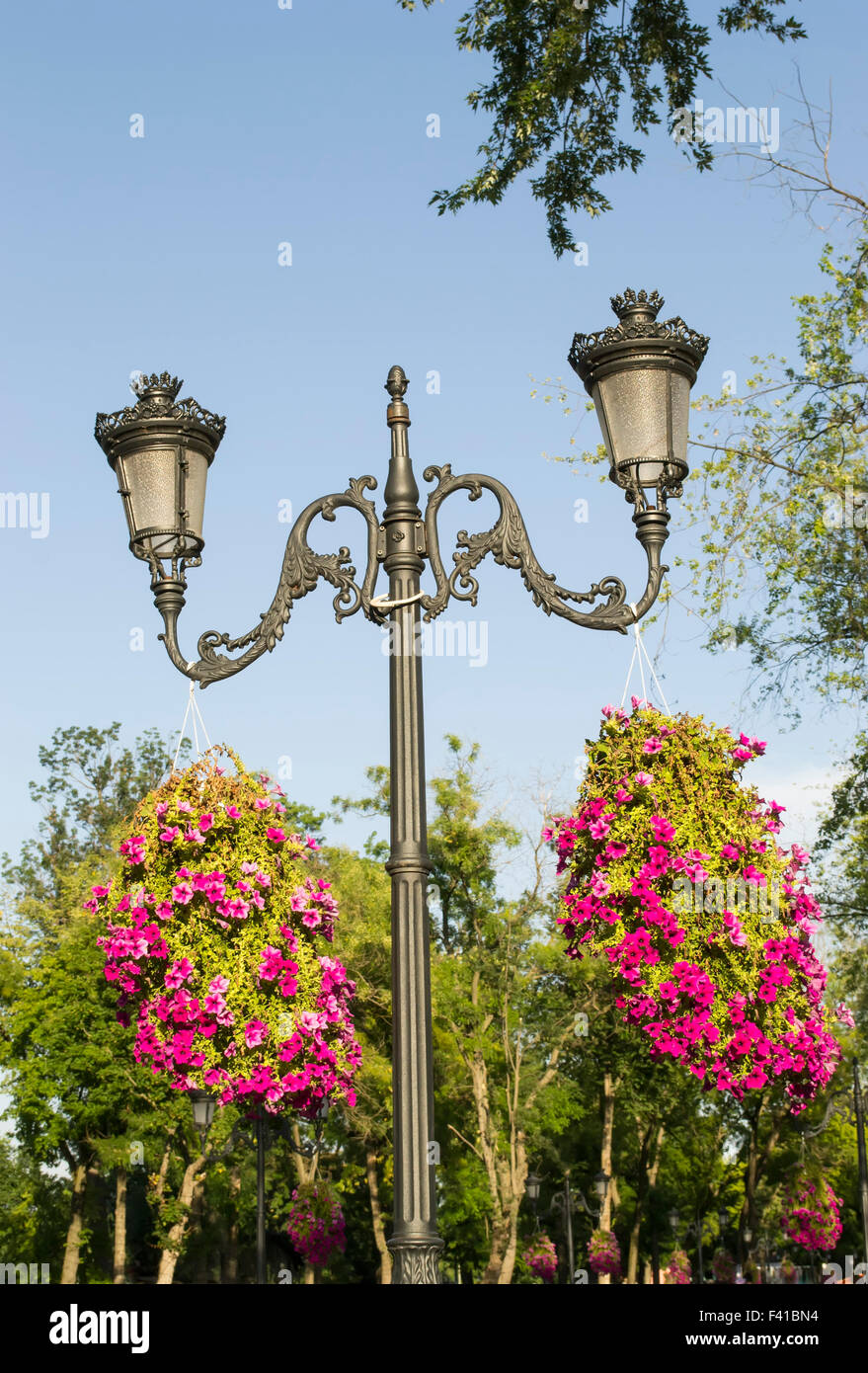 Strada elegante polo di illuminazione con due bracci e sbocciato appendere vasi da fiori in un parco Foto Stock