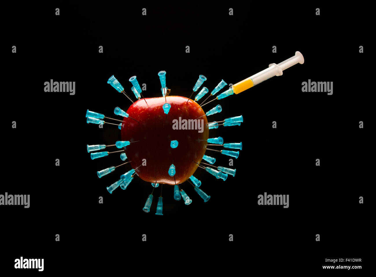 Una mela rossa piena di aghi ipodermici. Una siringa contenente fluido arancione è attaccata ad uno degli aghi. Isolato sul retro nero Foto Stock