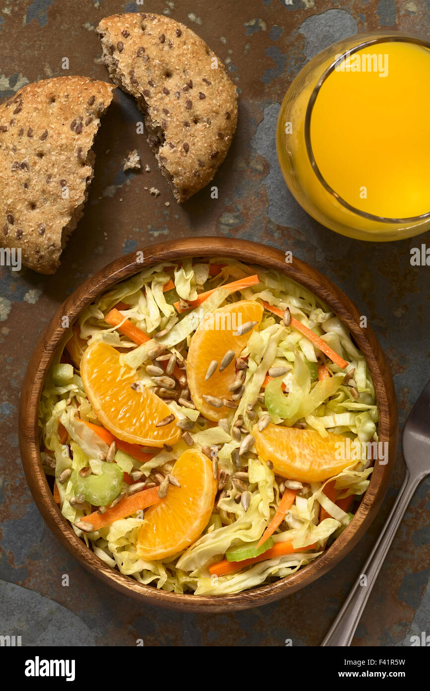 Insalata fresca fatta di cavolo verza, la carota e il sedano e arancione con arrosti di semi di girasole e servite nella ciotola di legno Foto Stock