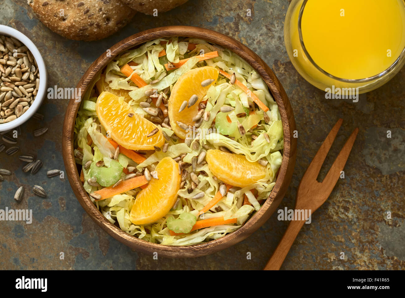 Insalata fresca fatta di cavolo verza, la carota e il sedano e arancione con arrosti di semi di girasole e servite nella ciotola di legno Foto Stock