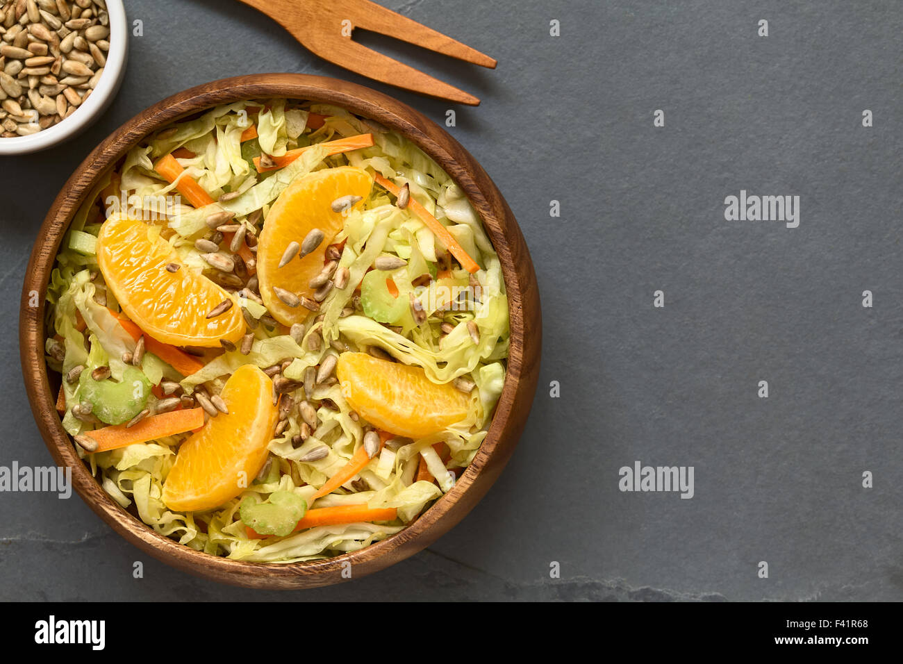 Insalata fresca fatta di cavolo verza, la carota e il sedano e arancione con arrosti di semi di girasole e servite nella ciotola di legno Foto Stock