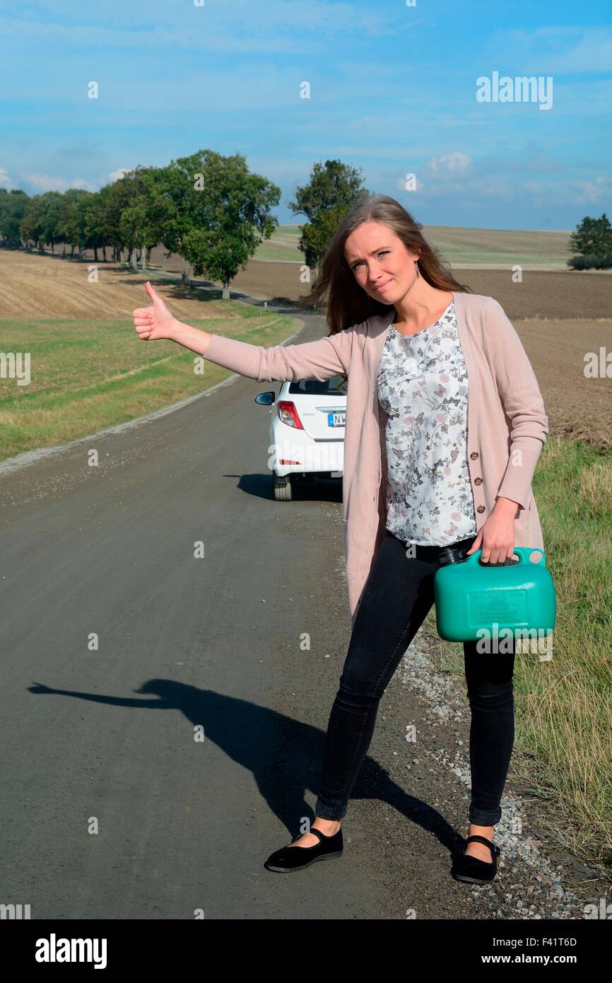 Bruna giovane donna tenendo un benzina può autostop su un vuoto che la strada di campagna, Krageholm, Skåne, sud della Svezia, Svezia Foto Stock