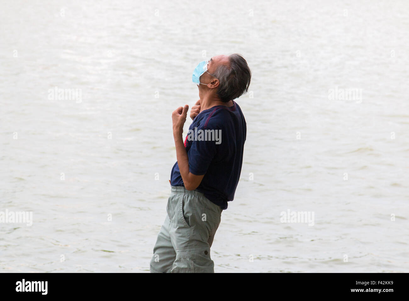 Il vietnamita uomo maturo praticare il tai chi sulla riva del lago Hoan Kiem ad Hanoi, maschera facciale contro l'inquinamento,Vietnam Foto Stock