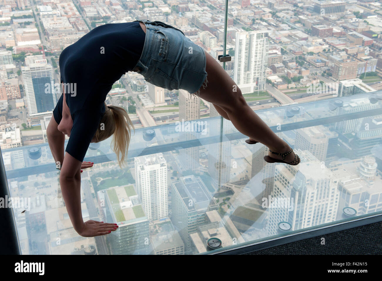 Donna facendo backbend in il fondo di vetro overservation coperta a Willis Tower, Chicago, Illinois, Stati Uniti d'America Foto Stock