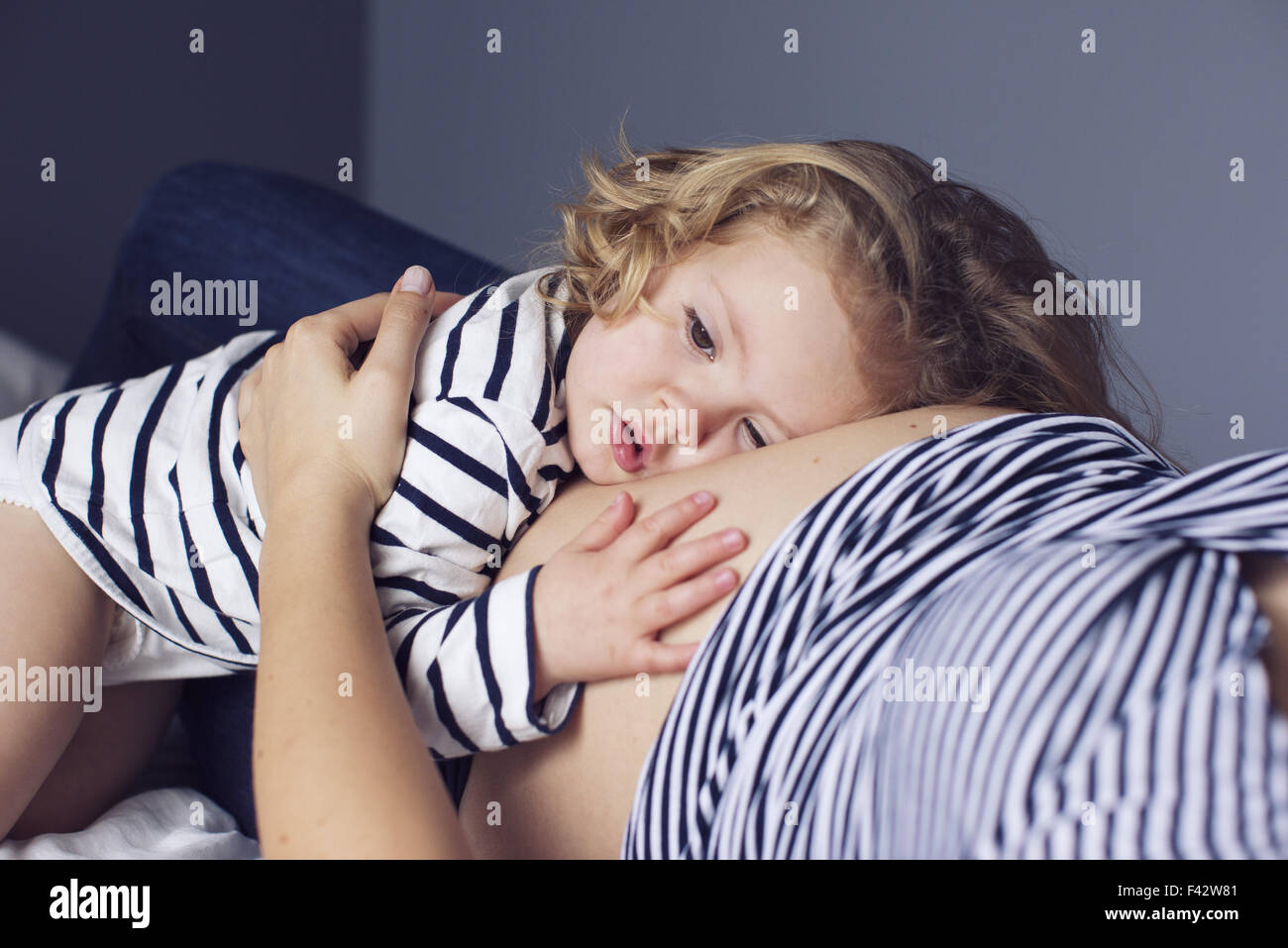 Bambina in appoggio la sua testa e la mano sulla madre di stomaco in gravidanza Foto Stock