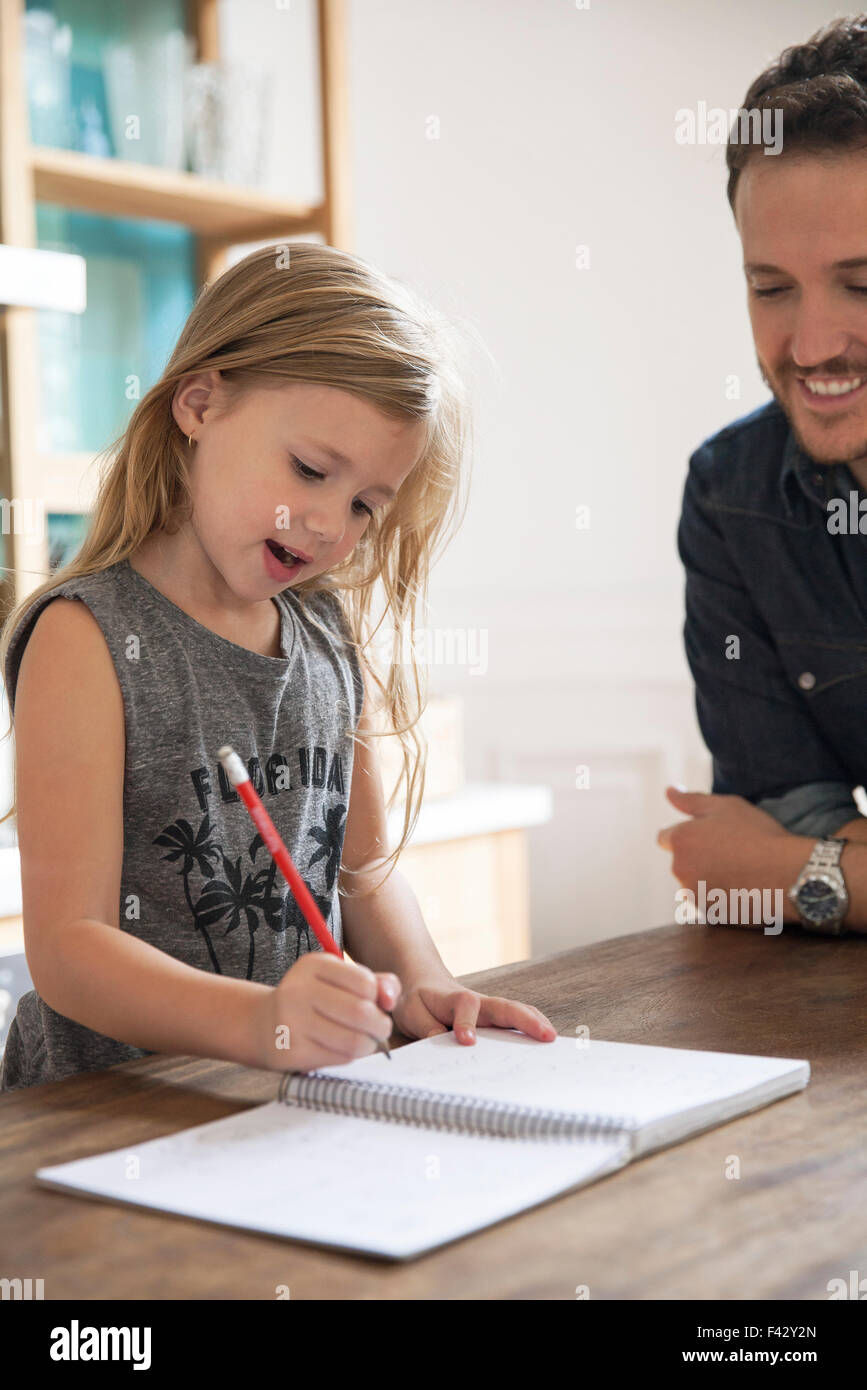 Padre guarda la giovane figlia pratica di scrittura Foto Stock