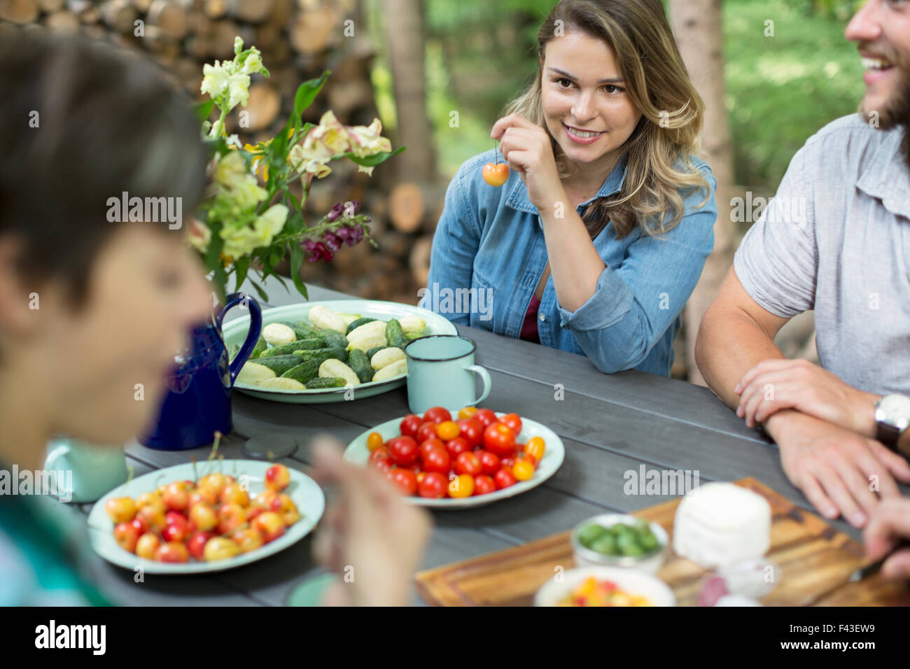 Tre persone sedute a un tavolo all'aperto, con frutta fresca e verdure in piatti sul tavolo. Foto Stock