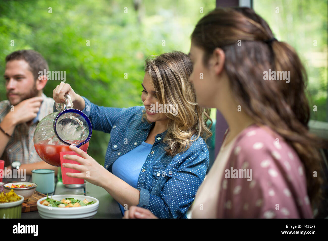 Tre persone sedute a un tavolo nel bosco, avente un pasto, una donna colata di succo da una caraffa. Foto Stock