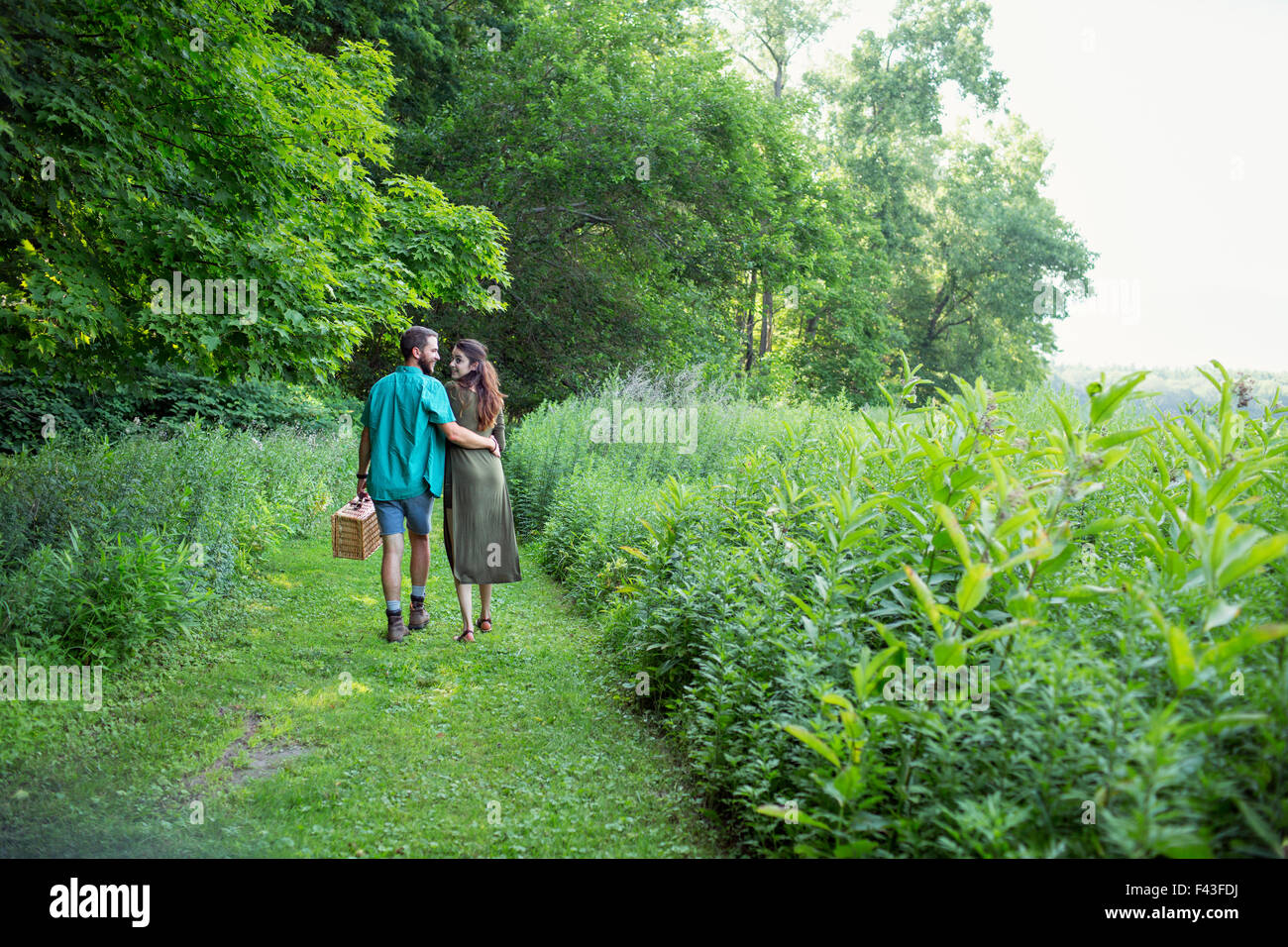 Un uomo e una donna a piedi attraverso un prato, attraverso l'erba lunga, portante un cestino da pic nic. Foto Stock