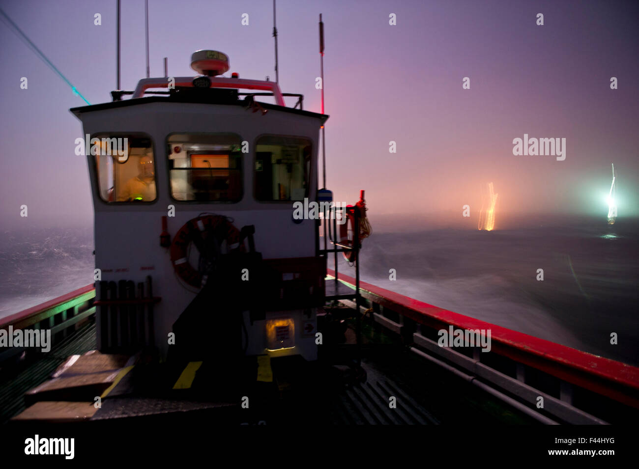 West coast rock'aragosta (Jasus lalandii) barca da pesca (James Archer) lascia il Saldhana Bay Harbor prima del break di Alba. Le luci della città e il faro flash all'orizzonte. Saldhana Bay, Western Cape, Sud Africa 2013. 3° premio nella Foto Stock