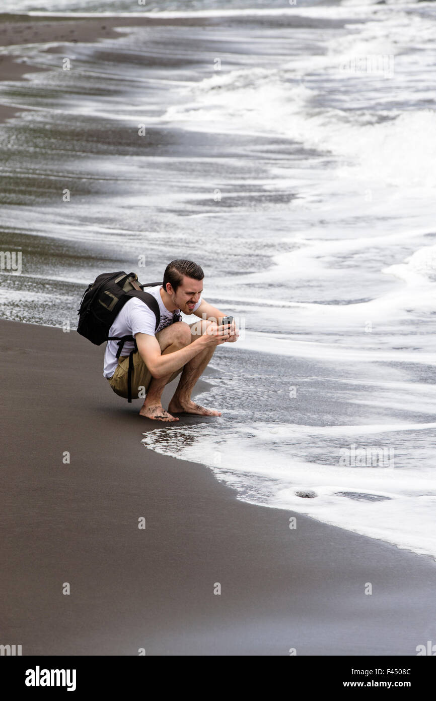 Turistica prendendo foto con il telefono sulla spiaggia al punto Akoakoa, Polulu Valley, Big Island delle Hawai'i, Hawai'i, STATI UNITI D'AMERICA Foto Stock