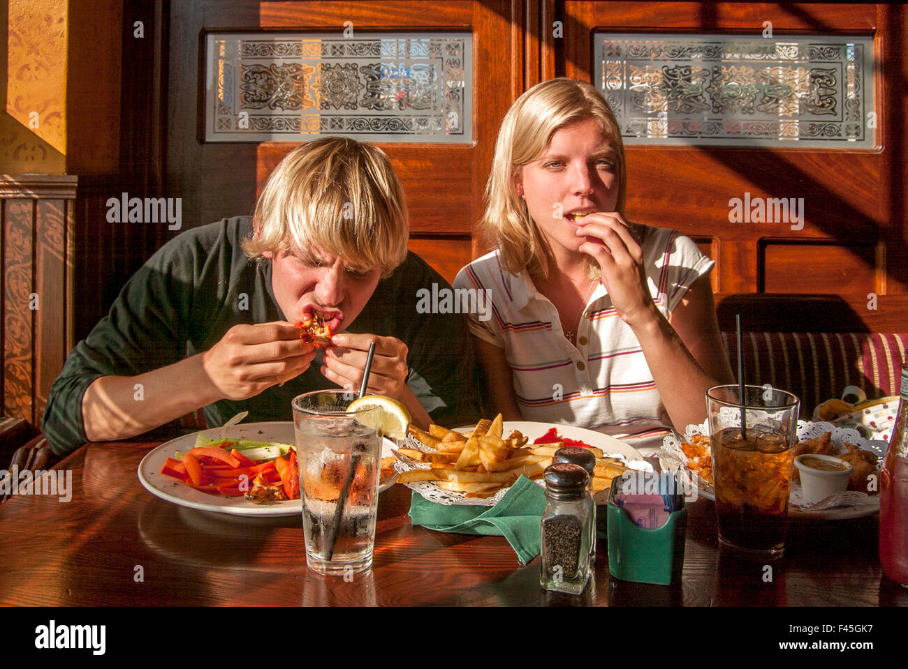 Due affamati bionda giovani adulti mangiare i frutti di mare a Huntington Beach, CA, porto ristorante stand. Foto Stock