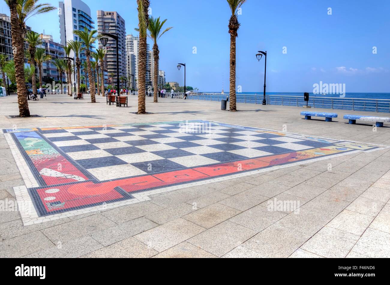 Una vista della Corniche a Beirut, in Libano e la scacchiera gigante verniciate sul pavimento. Una strada asfaltata fiancheggiata da palme Foto Stock