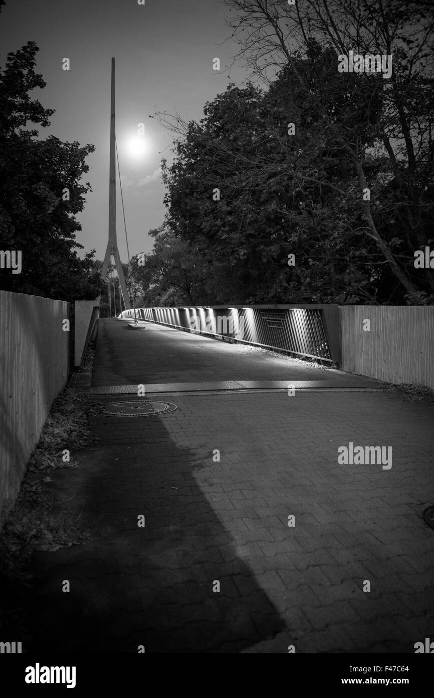 Viste in prospettiva di un ponte pedonale di Arco alto sopra la città autostrada a Berlino di notte alla luce della luna; monochrom Foto Stock