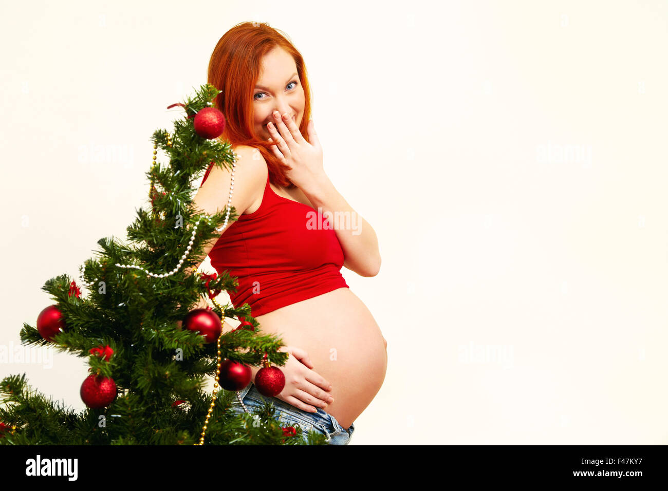Ritratto di un sorridente redhead donna incinta vicino all'albero di Natale Natale del popolo Foto Stock