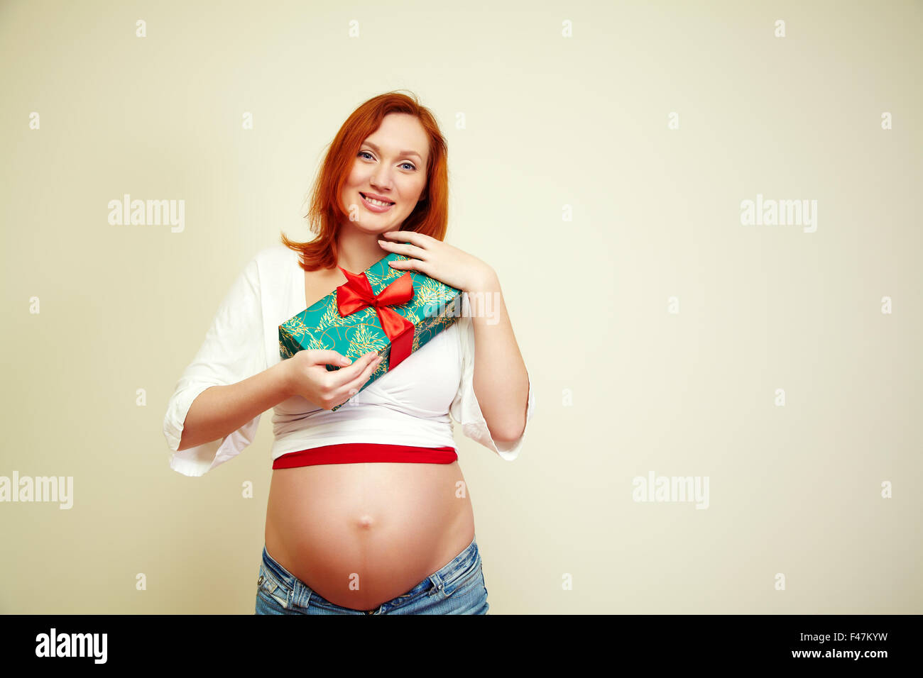 Ritratto di un sorridente redhead donna incinta con un regalo di Natale. persone Foto Stock