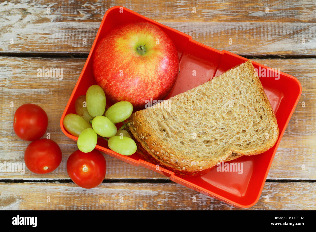 Scatola di pranzo marrone con sandwich di pane, mela rossa, uva e pomodorini Foto Stock