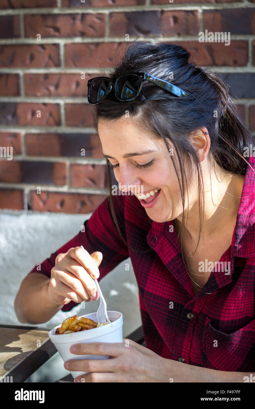 Felice giovani donne mangiare poutine quebec pasto fast food all'aperto nelle ore diurne Foto Stock