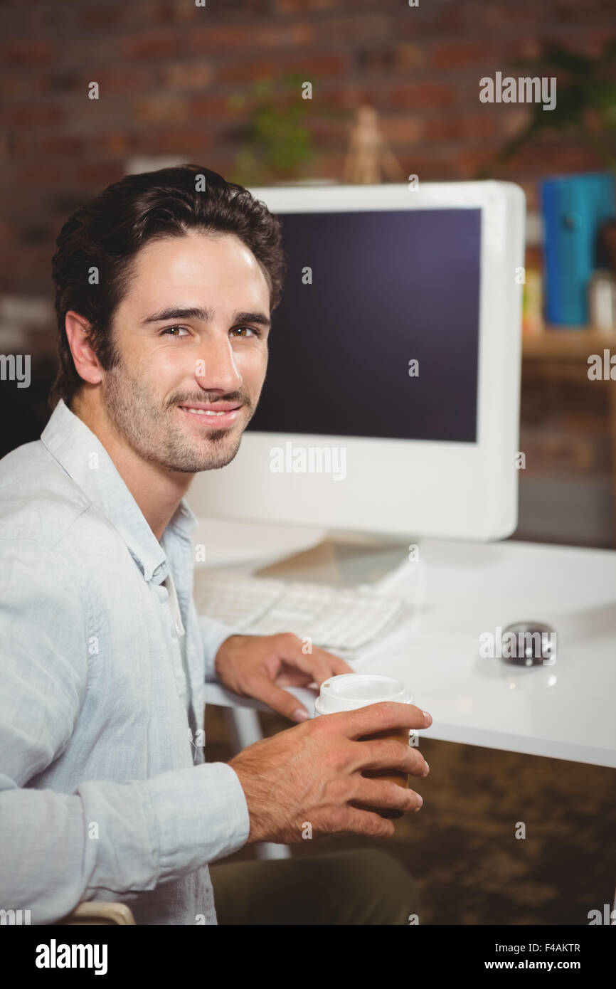 Sorridente giovane azienda caffè alla scrivania in ufficio Foto Stock