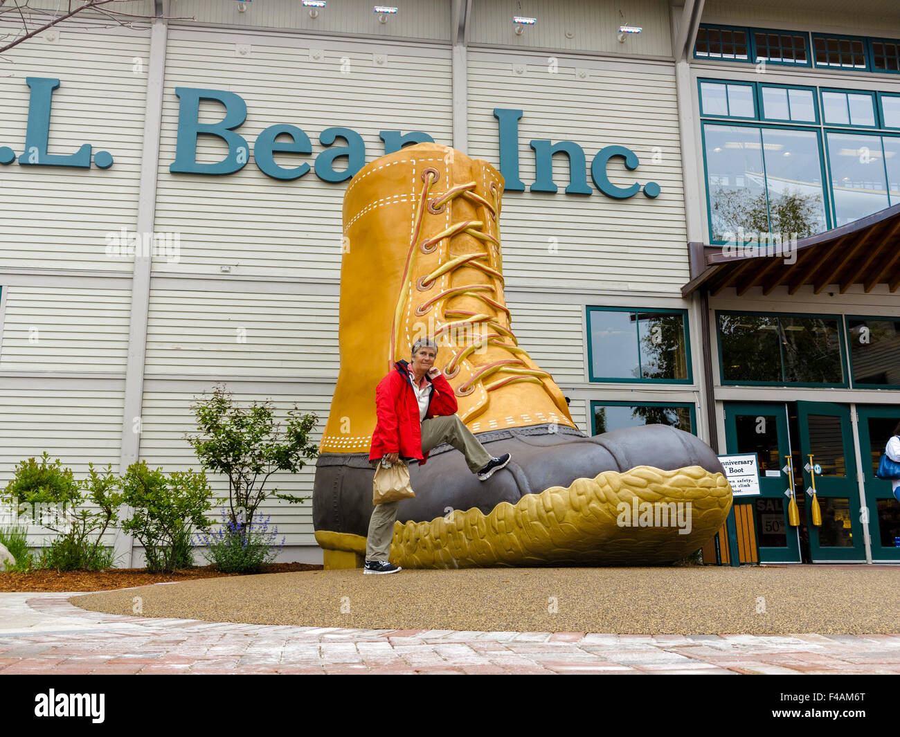 Donna appoggiata su un enorme L.L. Bean iconico boot al di fuori del loro negozio in Freeport, Maine Foto Stock