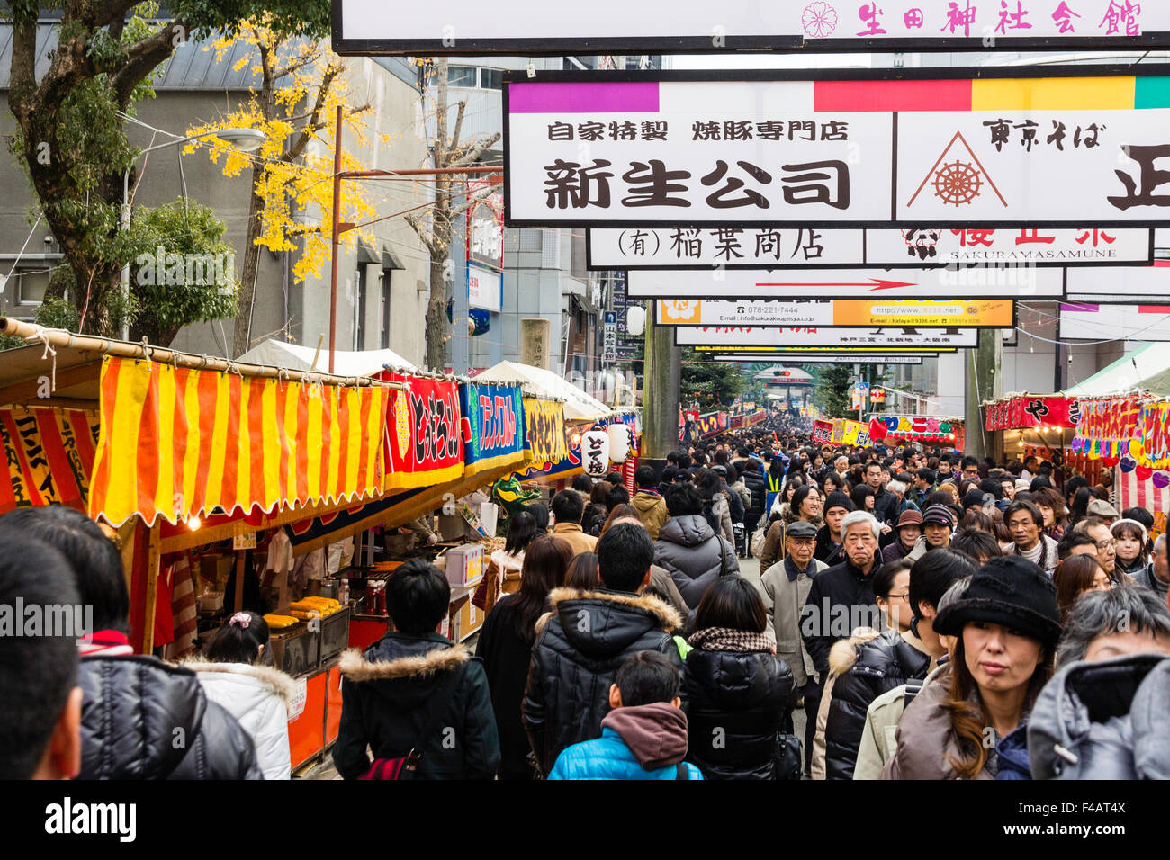 Ikuta santuario scintoista, Giappone durante Shogatsu, anno nuovo. La folla a piedi lungo avenue al santuario con bancarelle prodotti alimentari su entrambi i lati e sopra la testa la pubblicità. Foto Stock